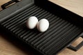 Black cast heavy iron grill pan in two organic white eggs; on modern oak kitchen countertop