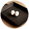 Black cast heavy iron grill pan in two organic white eggs on modern oak kitchen countertop