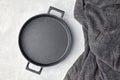 Black cast iron empty frying pan and gray kitchen towel on a gray concrete background Royalty Free Stock Photo