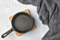 Black cast iron empty frying pan for one person on a wooden stand and a gray kitchen towel on a gray concrete background Royalty Free Stock Photo