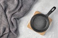 Black cast iron empty frying pan for one person on a wooden stand and a gray kitchen towel on a gray concrete background Royalty Free Stock Photo