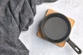 Black cast iron empty frying pan for one person on a wooden stand and a gray kitchen towel on a gray concrete background Royalty Free Stock Photo