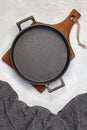 Black cast iron empty frying pan on a wooden cutting board and a gray kitchen towel on a gray concrete background Royalty Free Stock Photo