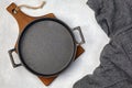 Black cast iron empty frying pan on a wooden cutting board and a gray kitchen towel on a gray concrete background Royalty Free Stock Photo