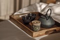 Black cast iron tea pot with herbal tea set up on wood tray on the bed. Royalty Free Stock Photo