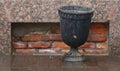 Black cast-iron trash can by a brick-lined basement window