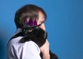 Cat in pink shiny crown sitting on man sholder with extended paws on blue background Royalty Free Stock Photo