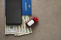 Black cellphone, money American dollars banknotes bills, passport and toy car on copy space background, top view. Travel light,