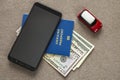 Black cellphone, money American dollars banknotes bills, passport and toy car on copy space background, top view. Travel light, Royalty Free Stock Photo