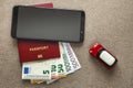 Black cellphone, money euro banknotes bills, passport and toy car on copy space background. Travel light, comfortable journey
