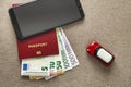 Black cellphone, money euro banknotes bills, passport and toy car on copy space background. Travel light, comfortable journey