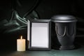 Black cemetery urn with black mourning frame, burning candle, on deep green background