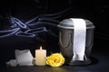 Black cemetery urn with burning candle and white ribbon yellow rose on deep blue background Royalty Free Stock Photo