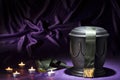 Black cemetery urn with candles, and deep green ribbon on dark purple background Royalty Free Stock Photo