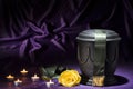Black cemetery urn with candles yellow rose, and dark green ribbon, on deep purple background Royalty Free Stock Photo