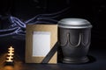 Black cemetery urn with wooden mourning frame burning candles, on deep blue background Royalty Free Stock Photo