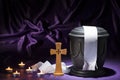 Black cemetery urnk with cross and candles and white ribbon on deep purple background