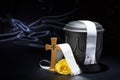 Black cemetery urnk with cross, white ribbon, yellow rose, on deep blue background Royalty Free Stock Photo