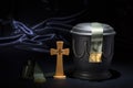 Black cemetery urnk with wooden cross, deep green ribbon, on dark blue background Royalty Free Stock Photo