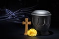 Black cemetery urnk with wooden cross, yellow rose on deep blue background