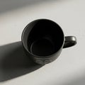 A black ceramic mug is positioned upright on a light gray, textured counte Royalty Free Stock Photo