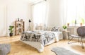 Black chair near bed with patterned sheets in white bedroom interior with pouf and fur. Real photo Royalty Free Stock Photo