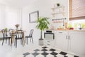 Black chairs at dining table with flowers in white flat interior with plant next to kitchenette. Real photo