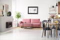 Black chairs at table with flowers in spacious flat interior with poster above pink sofa. Real photo Royalty Free Stock Photo