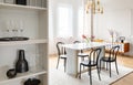 Black chairs at table with flowers under gold lamp in white modern dining room interior. Real photo