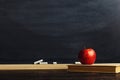 Black chalk board over wooden table with a book and an apple, blank for text or background for a school theme Royalty Free Stock Photo