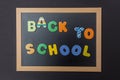 Black chalkboard with wooden frame, text back to school in colorful letters, black wall background