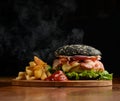 Black cheese burger with bacon onion tomatoes and french fries on wooden rustic cutting board