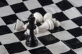 Black chess king standing on chessboard, white king fallen with