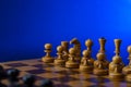 Black chess pieces against white chess pieces on a chessboard on a blue background with place for text Royalty Free Stock Photo