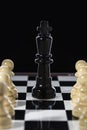 Black chess queen and army of white pawns on a chessboard on a black background