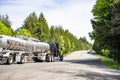 Black classic big rig bonnet semi truck tractor transporting liquid cargo in long tank semi trailer running on the divided wide Royalty Free Stock Photo