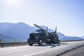 Black classic big rig semi truck with semi trailer for transportation wood logs running on the road along Columbia River in