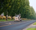 Black classic bonnet big rig semi truck with vertical pipes going on divided road with green trees