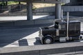 Black classic powerful big rig semi truck running on the highway under the bridge Royalty Free Stock Photo