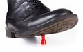 Black classy boot stomping and crushing a small red pawn game piece under sole. Big vs small, power, danger and helplessness Royalty Free Stock Photo