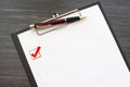 Black clipboard with white sheet of paper and metal pen isolated on dark wooden table. Checkbox with a tick on the page Royalty Free Stock Photo