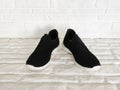 Black cloth sports sneakers with white soles on white brick background