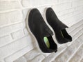 Black cloth sports sneakers with white soles on white brick background