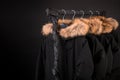 Black coats, jacket with fur on hood hanging clothes rack. background. Copy space.