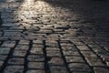 Black cobbled stone road background with reflection of light seen on the road. Black or dark grey stone pavement texture.