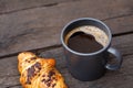 Black coffee in a blue-grey ceramic mug next to chocolate croissant isolated on rustic dark brown wood table Royalty Free Stock Photo