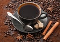 Black coffee in ceramic cup with cinnamon and cane sugar with anise star and silver spoon on ground coffee and beans Royalty Free Stock Photo