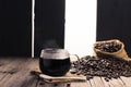 Black coffee in a cup of coffee with hot steam and coffee beans placed on a wooden table on a dark background. in a warm Royalty Free Stock Photo