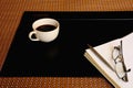 Black coffee cup, notebook, pen, eyeglass and Black vinyl desk pad on brown mat Royalty Free Stock Photo