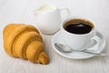 Black coffee in cup, spoon on saucer, croissant, milk Royalty Free Stock Photo